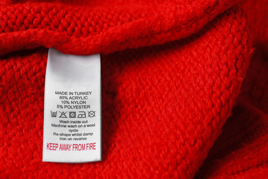 Photo of Clothing label with care symbols and material content on red sweater, closeup view