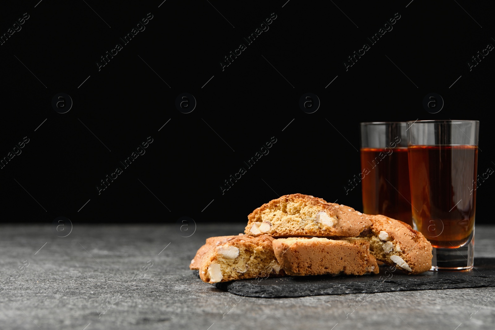 Photo of Tasty cantucci and glasses of liqueur on grey table, space for text. Traditional Italian almond biscuits