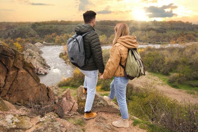 Photo of Couple of hikers with travel backpacks enjoying beautiful view near mountain river