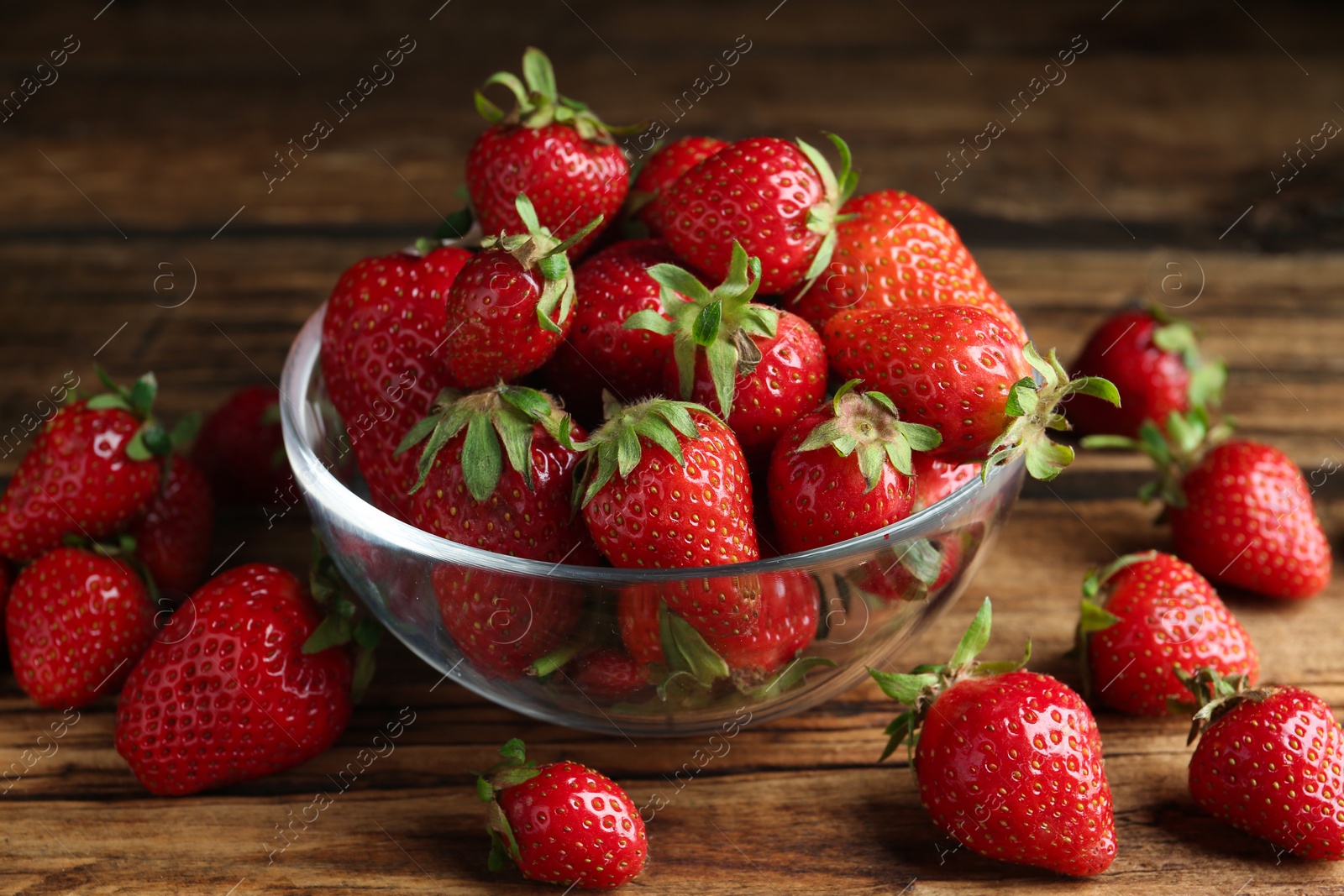 Photo of Delicious ripe strawberries in glass bowl on wooden table