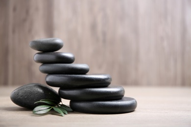 Photo of Black spa stones with branch on wooden background. Space for text