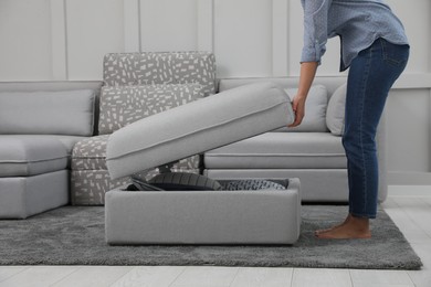 Photo of Woman opening modular sofa section with storage in living room, closeup