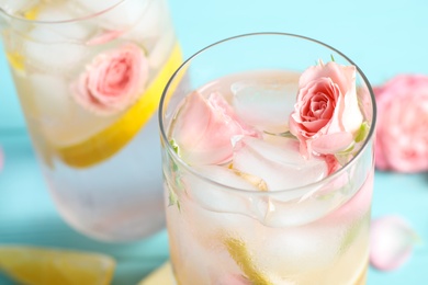 Photo of Tasty refreshing lemon drink with roses on light blue table, closeup
