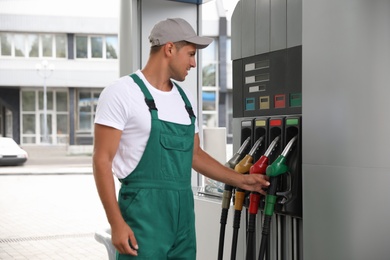 Photo of Worker taking fuel pump nozzle at modern gas station