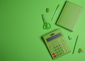 Flat lay composition with stationery and calculator on green background. Space for text