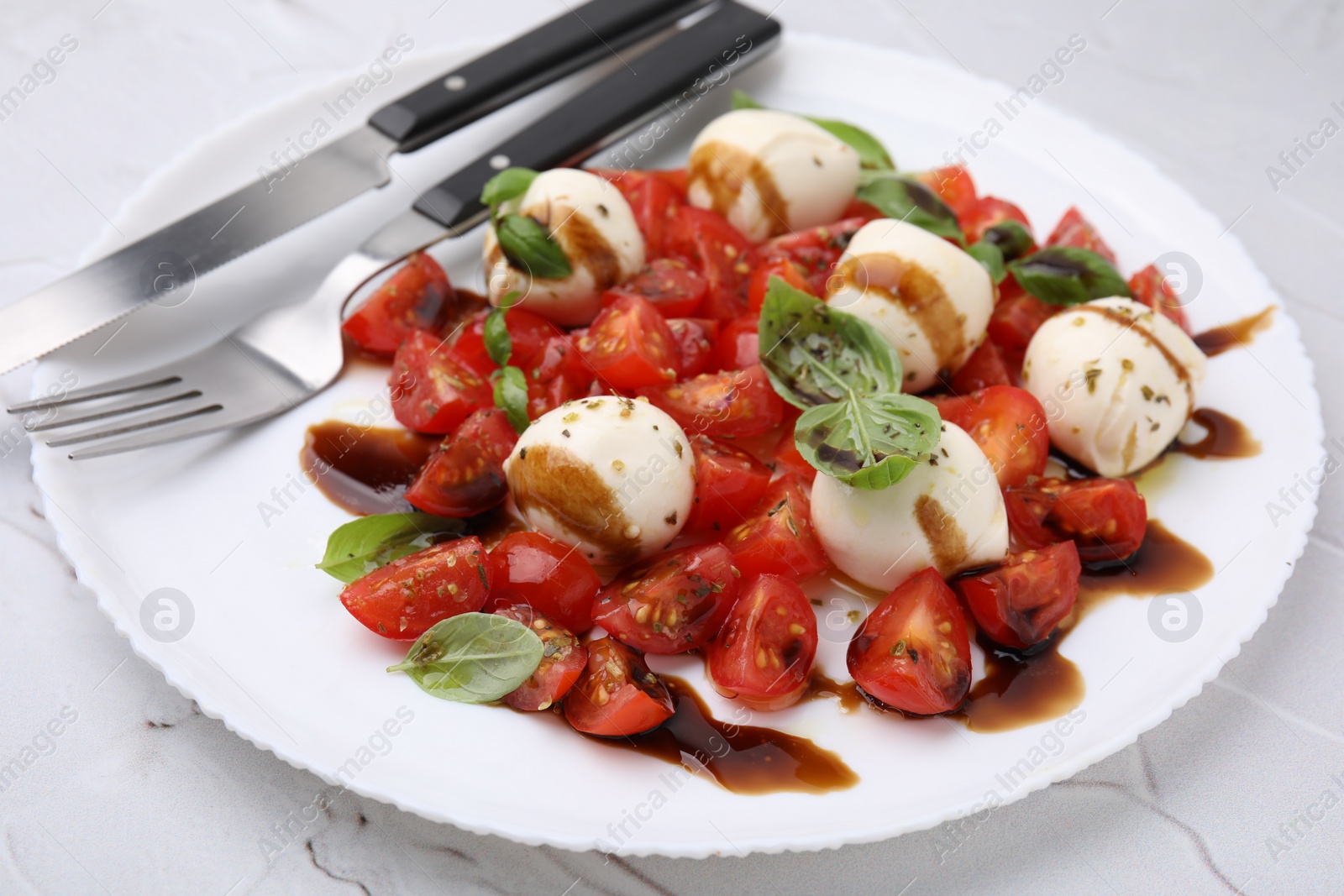 Photo of Tasty salad Caprese with tomatoes, mozzarella balls, basil and cutlery on white table, closeup