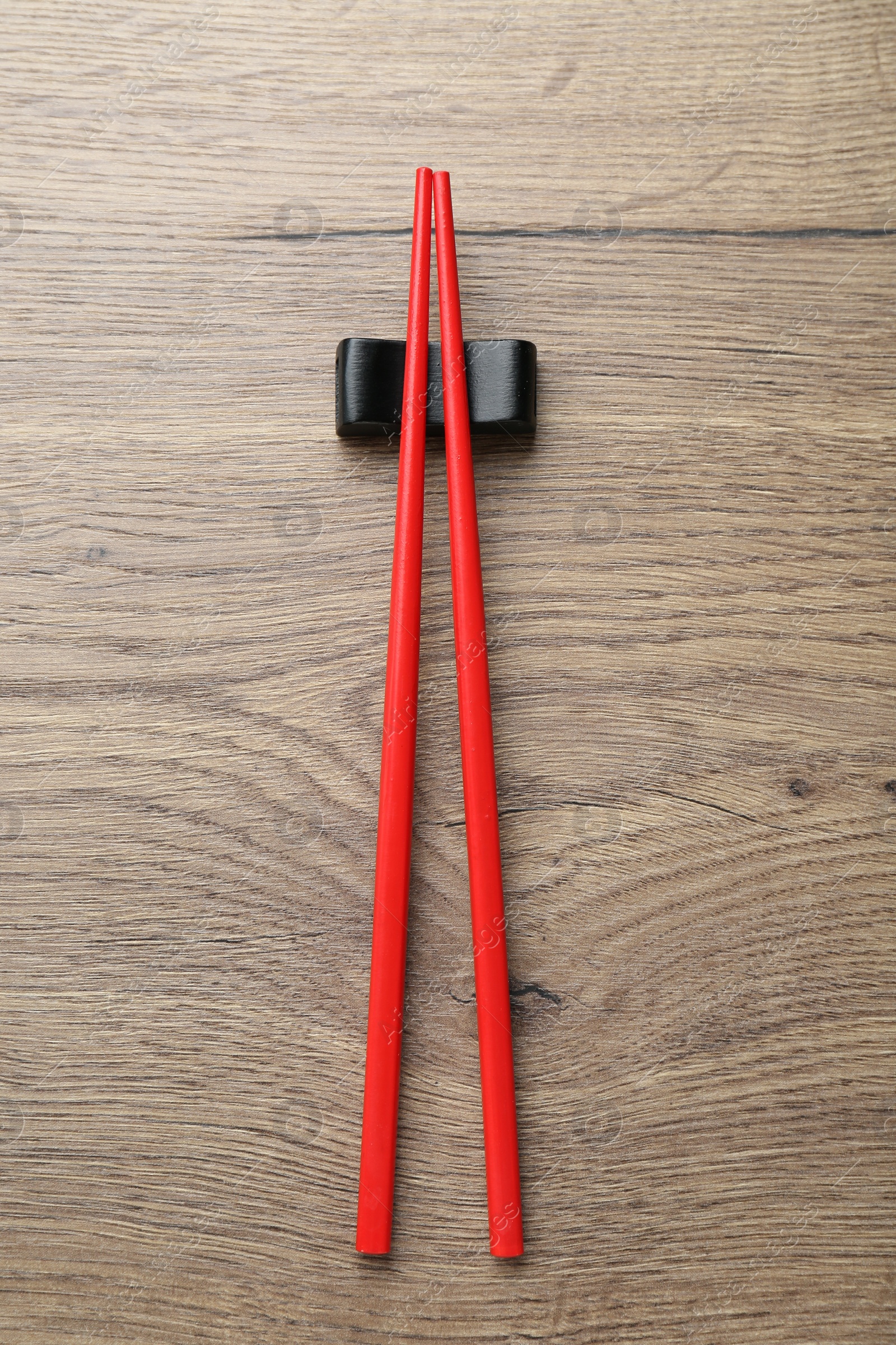 Photo of Pair of red chopsticks with rest on wooden table, top view