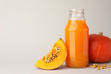Tasty pumpkin juice in glass bottle, whole and cut pumpkins on light background. Space for text