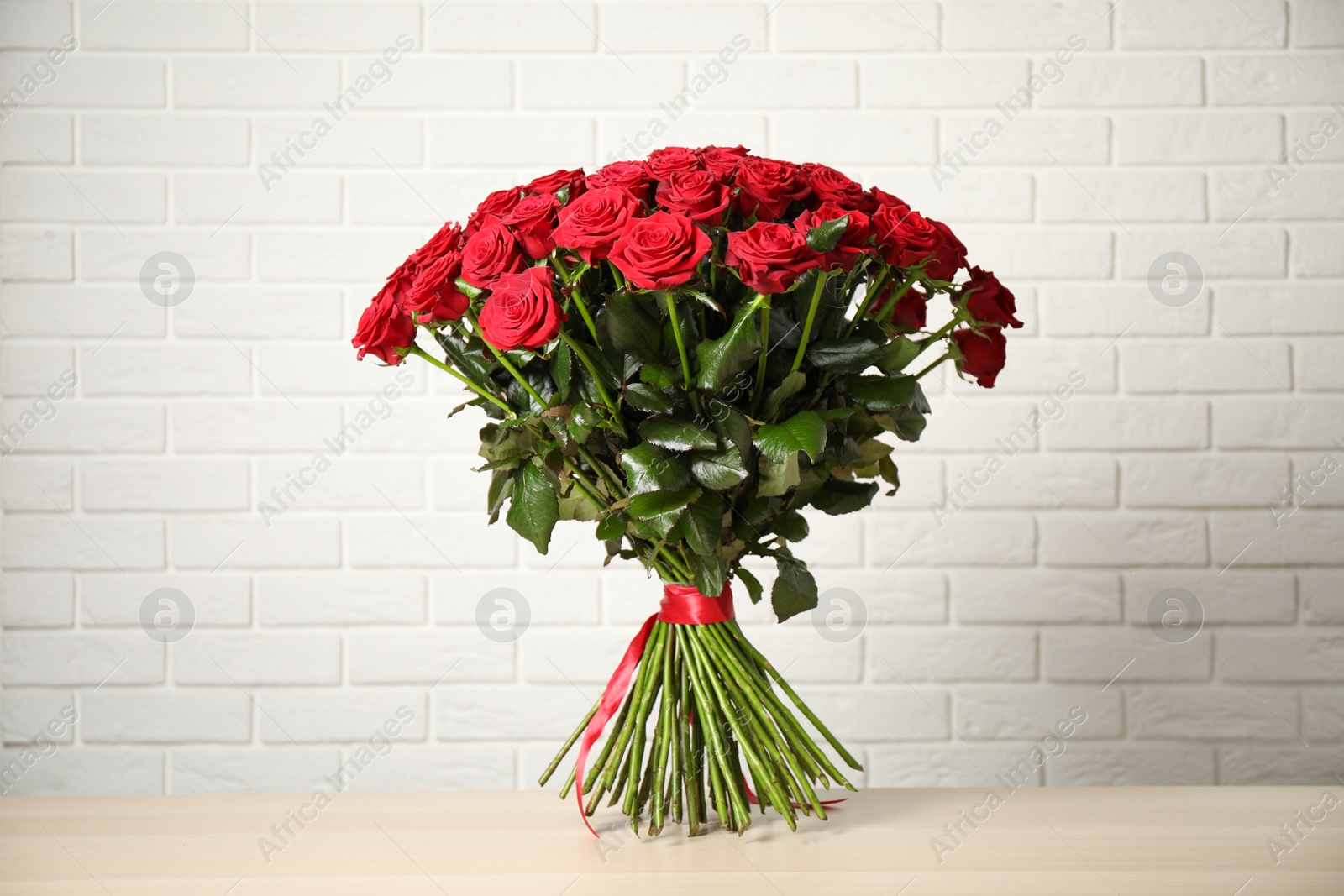 Photo of Luxury bouquet of fresh red roses on wooden table near white brick wall
