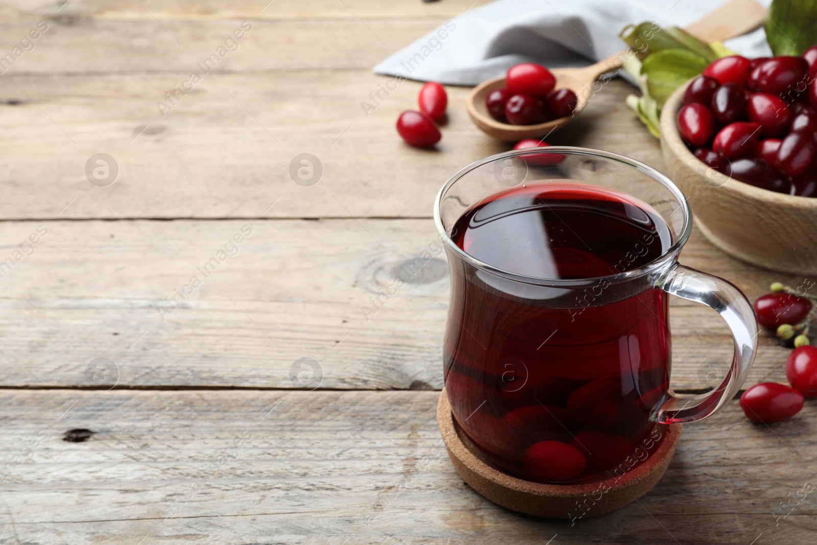 Photo of Glass cup of fresh dogwood tea with berries on wooden table. Space for text