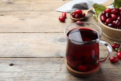 Photo of Glass cup of fresh dogwood tea with berries on wooden table. Space for text