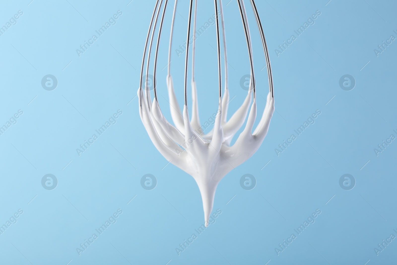 Photo of Whisk with whipped cream on light blue background, closeup