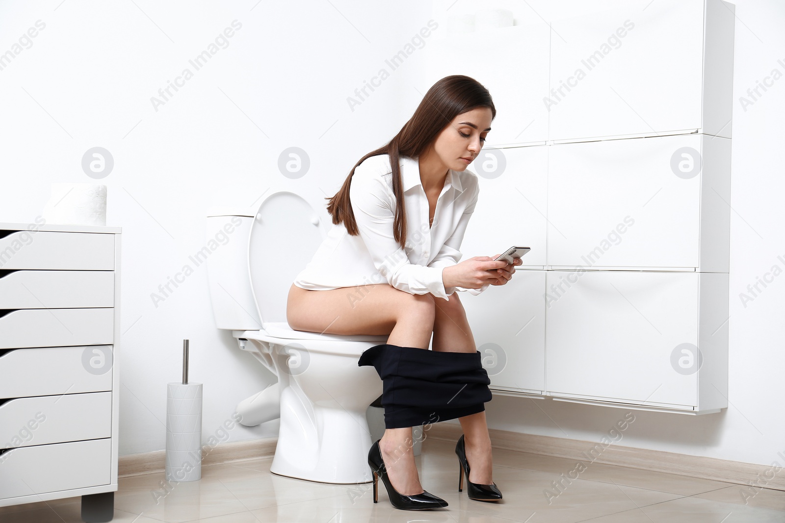 Photo of Woman with smartphone sitting on toilet bowl in bathroom