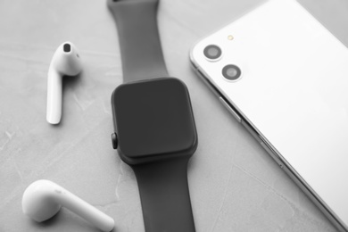 Photo of Stylish smart watch, phone and earphones on grey stone table, closeup