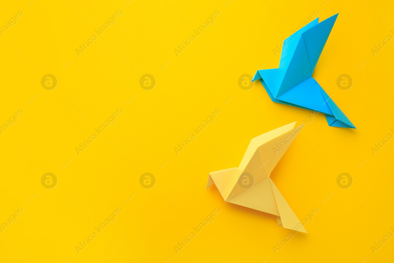 Photo of Origami art. Colorful handmade paper birds on yellow background, flat lay. Space for text