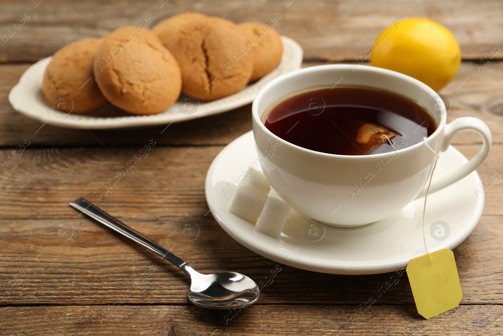 Photo of Tea bag in ceramic cup of hot water and cookies on wooden table