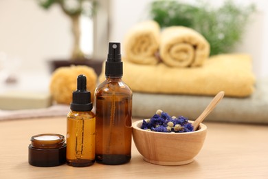 Photo of Bottles of essential oils, dry flowers and jar with cream on light wooden table. Spa therapy