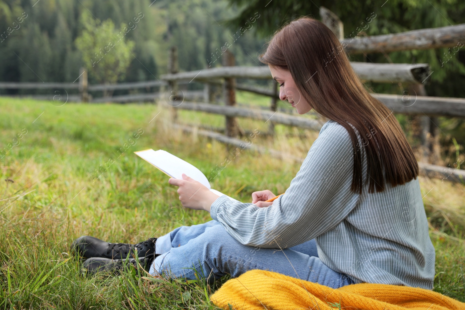 Photo of Beautiful young woman drawing with pencil in notepad on green grass