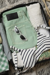 Photo of Open suitcase with summer clothes and sunglasses on floor, top view