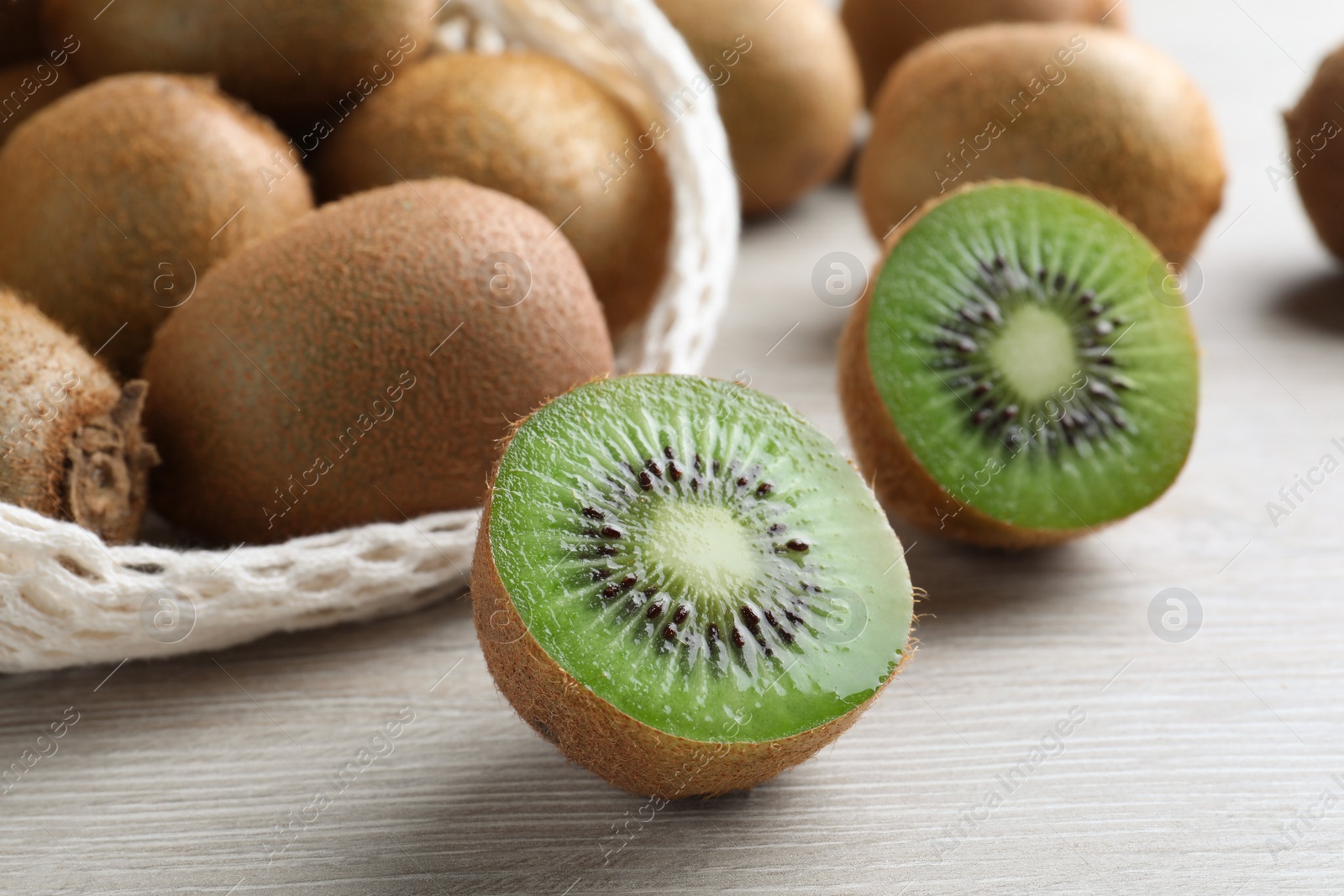 Photo of Cut and whole fresh kiwis on white wooden table, closeup