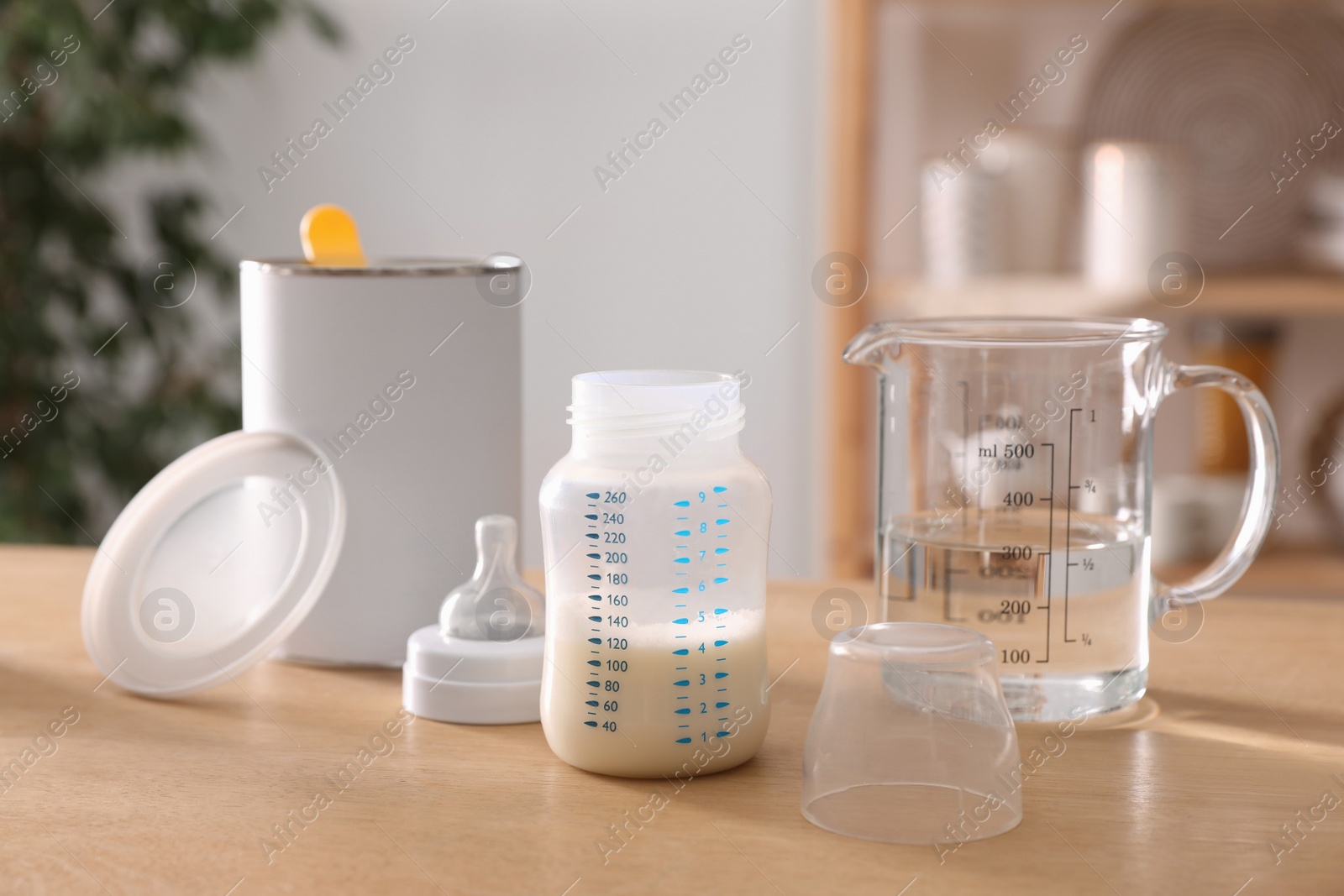 Photo of Feeding bottle with infant formula, can and jug of water on wooden table indoors. Baby milk