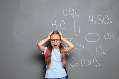 Photo of Little school child with backpack and chemical formulas on grey background