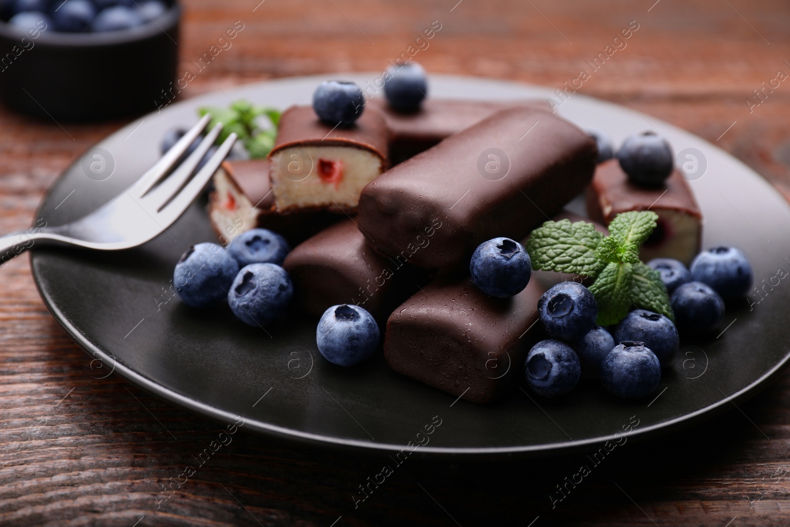 Photo of Delicious glazed curd snacks with fresh blueberries and mint served on wooden table, closeup