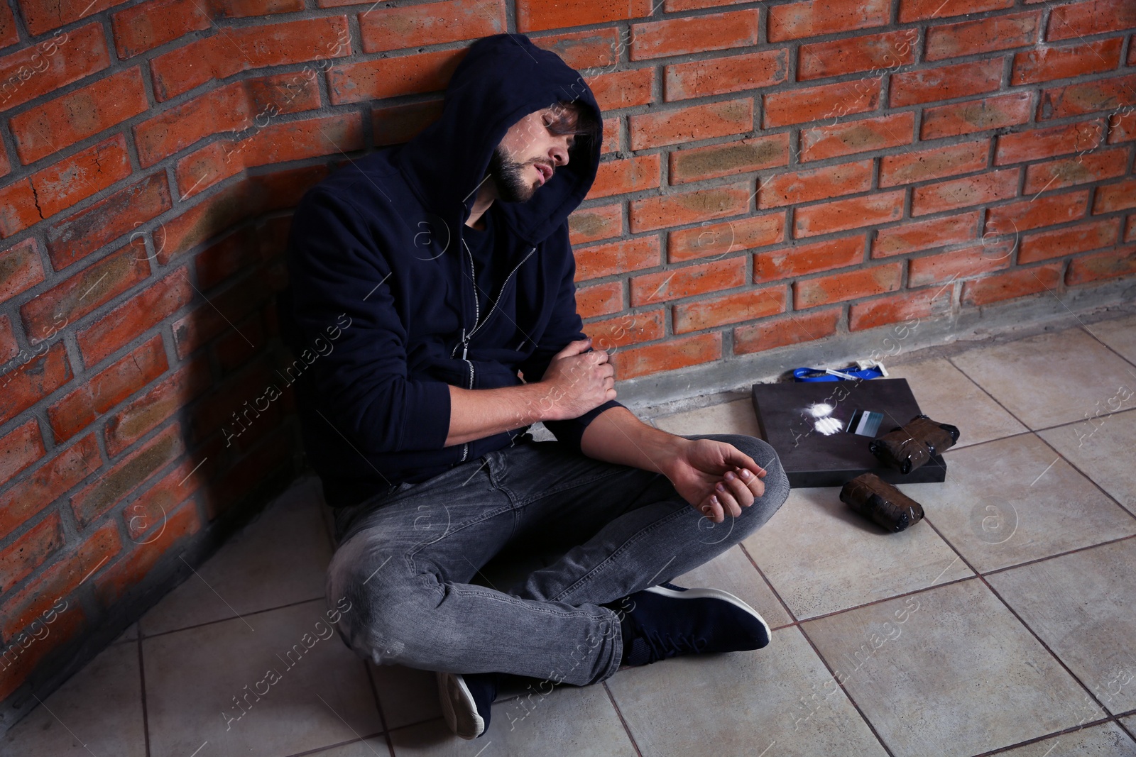 Photo of Young addicted man sitting near brick wall after using drugs