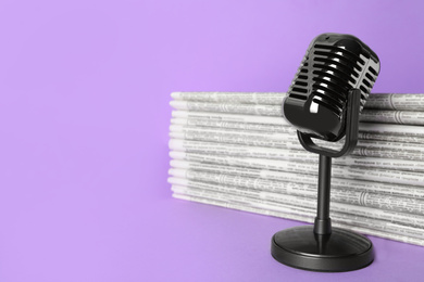 Newspapers and vintage microphone on light violet background, space for text. Journalist's work