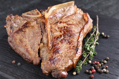 Photo of Delicious fried beef meat, thyme and peppercorns on wooden board, closeup