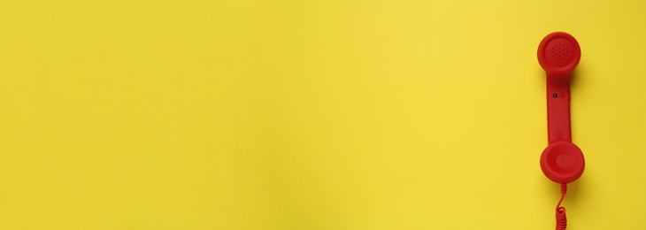 Image of Hotline service. Red telephone receiver and space for text on yellow background, top view