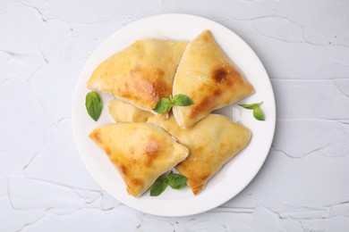 Delicious samosas and basil on white textured table, top view