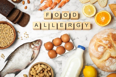 Photo of Flat lay composition of different products and wooden cubes with words Food Allergy on white marble table