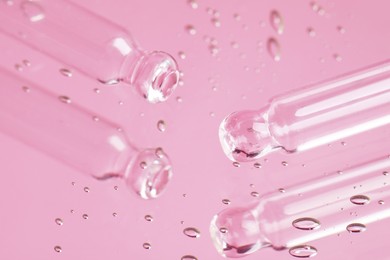 Pipettes near serum drops on beautiful mirror, closeup. Toned in pink