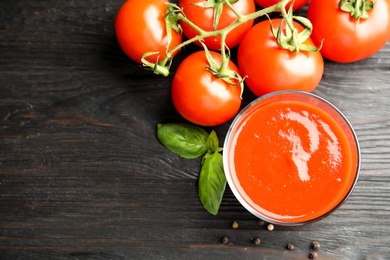 Photo of Glass of sauce and tomatoes with basil on wooden table, top view. Space for text