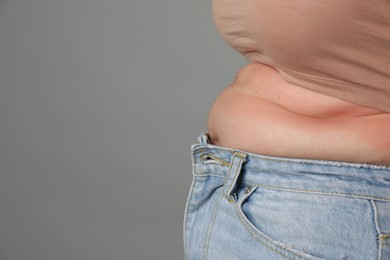 Photo of Overweight woman in tight jeans on grey background, closeup. Space for text