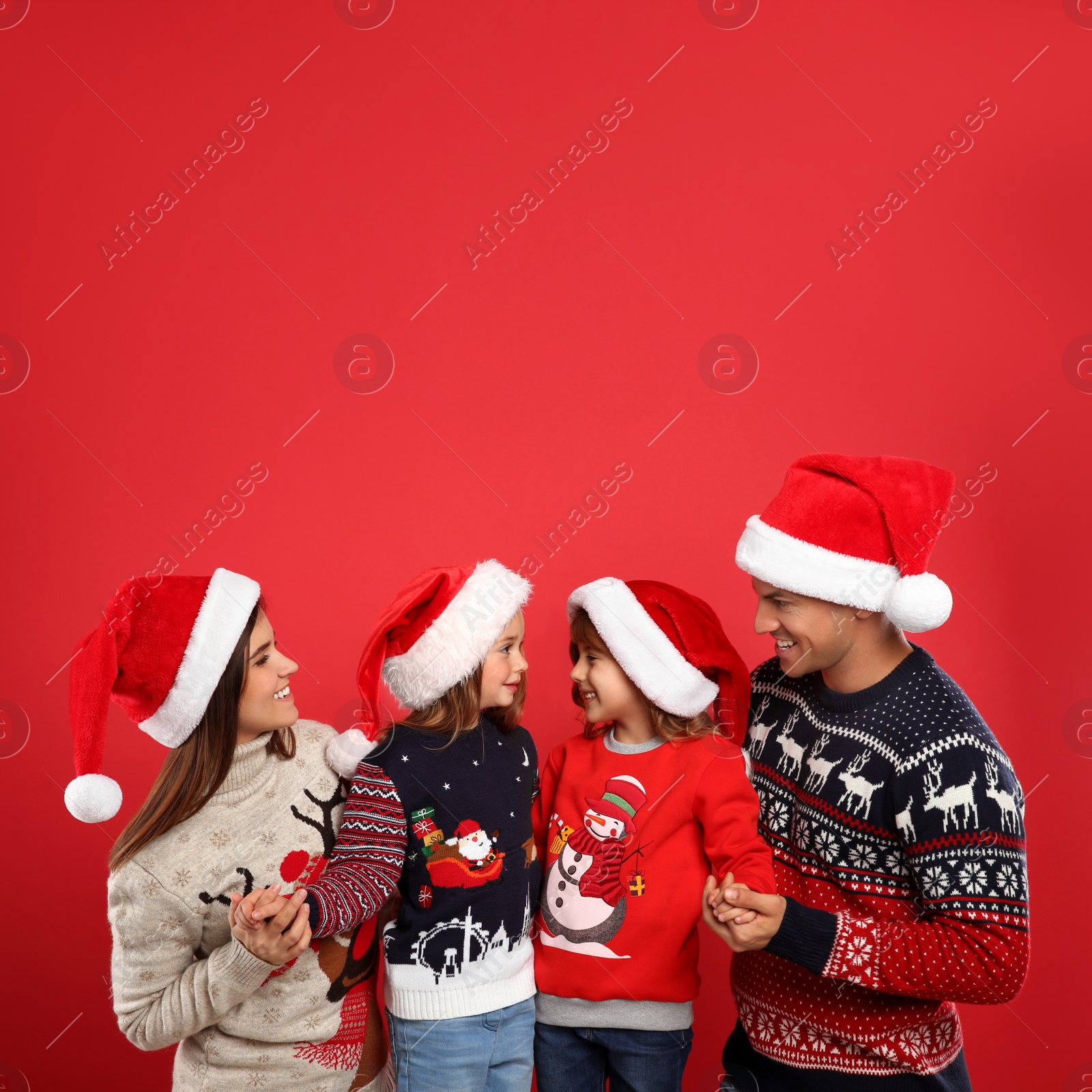 Photo of Family in Christmas sweaters and Santa hats on red background