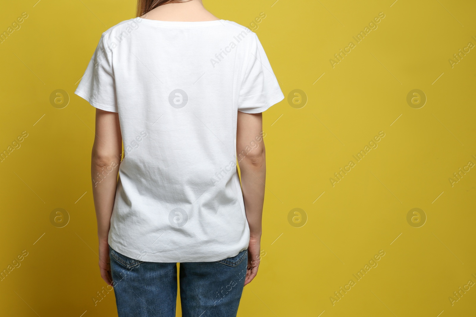 Photo of Back view of young woman wearing blank t-shirt on yellow background, closeup. Mockup for design