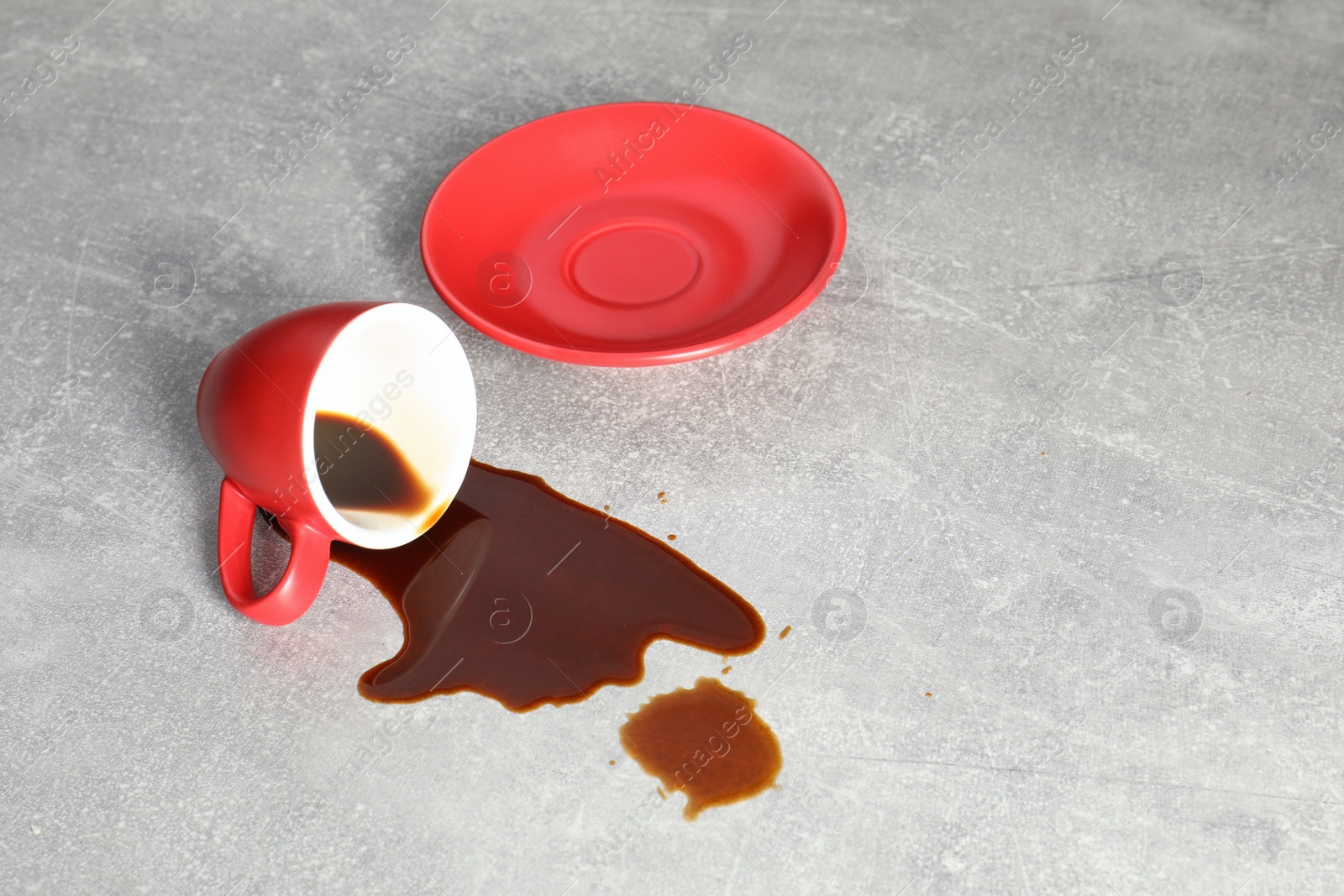 Photo of Cup with saucer and coffee spill on grey table. Space for text