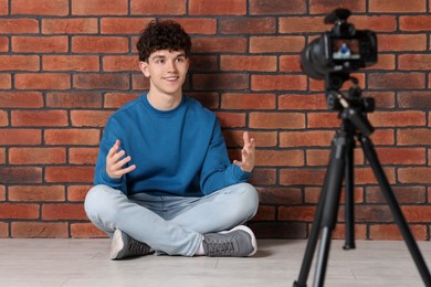 Photo of Smiling teenage blogger explaining something while streaming indoors