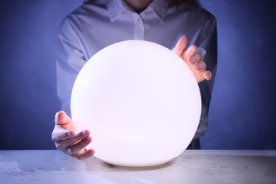 Photo of Businesswoman using glowing crystal ball to predict future at table, closeup. Fortune telling
