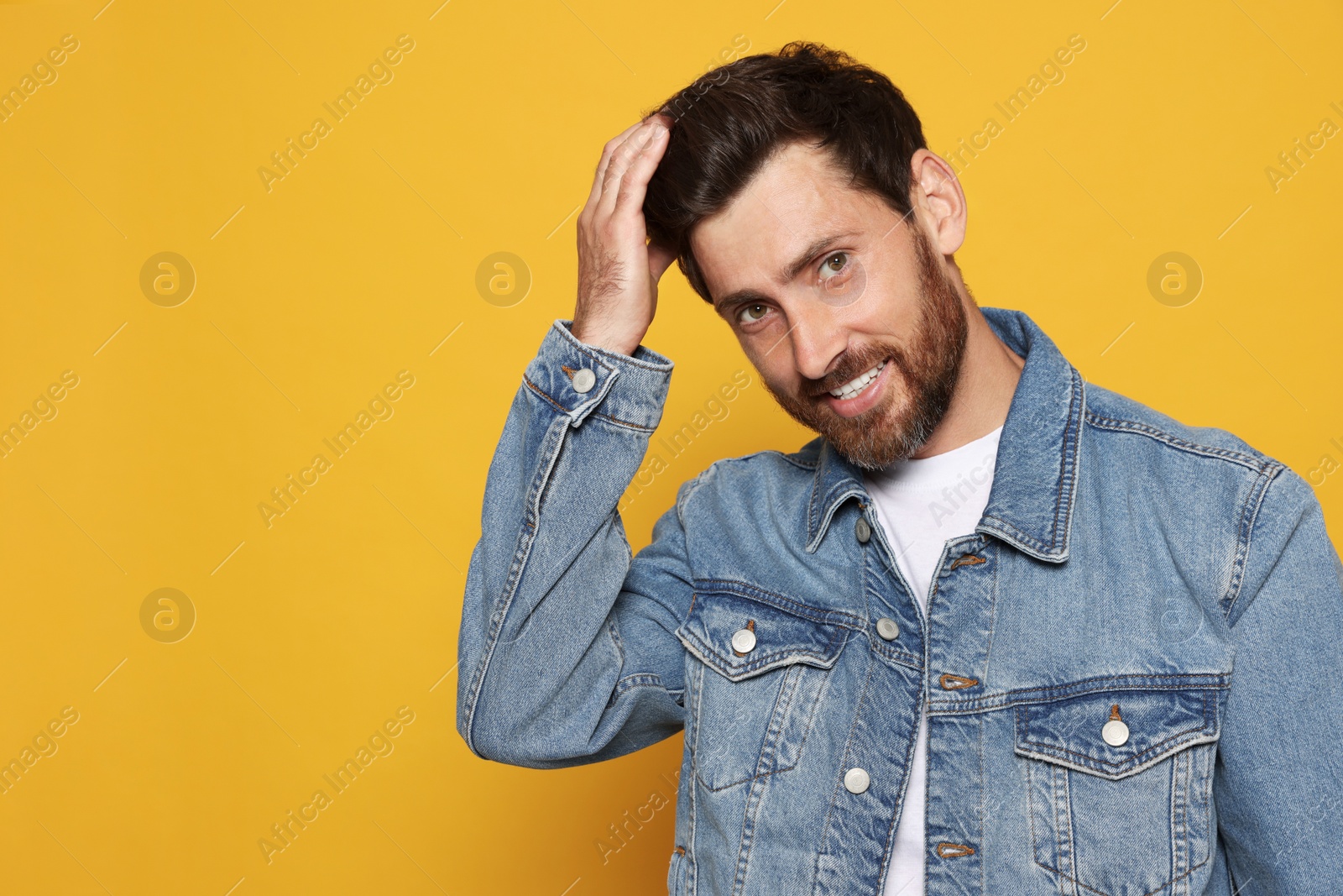 Photo of Bearded man fixing hair on orange background. Space for text