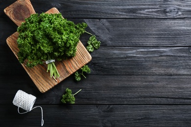 Photo of Fresh curly parsley, cutting board and rope on black wooden table, flat lay. Space for text