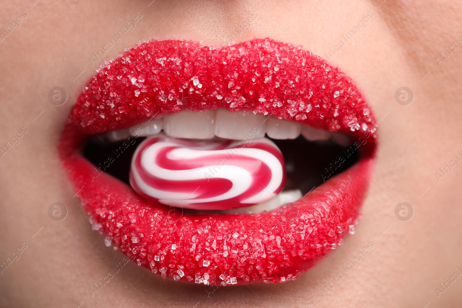 Photo of Young woman with beautiful lips covered in sugar eating candy, closeup