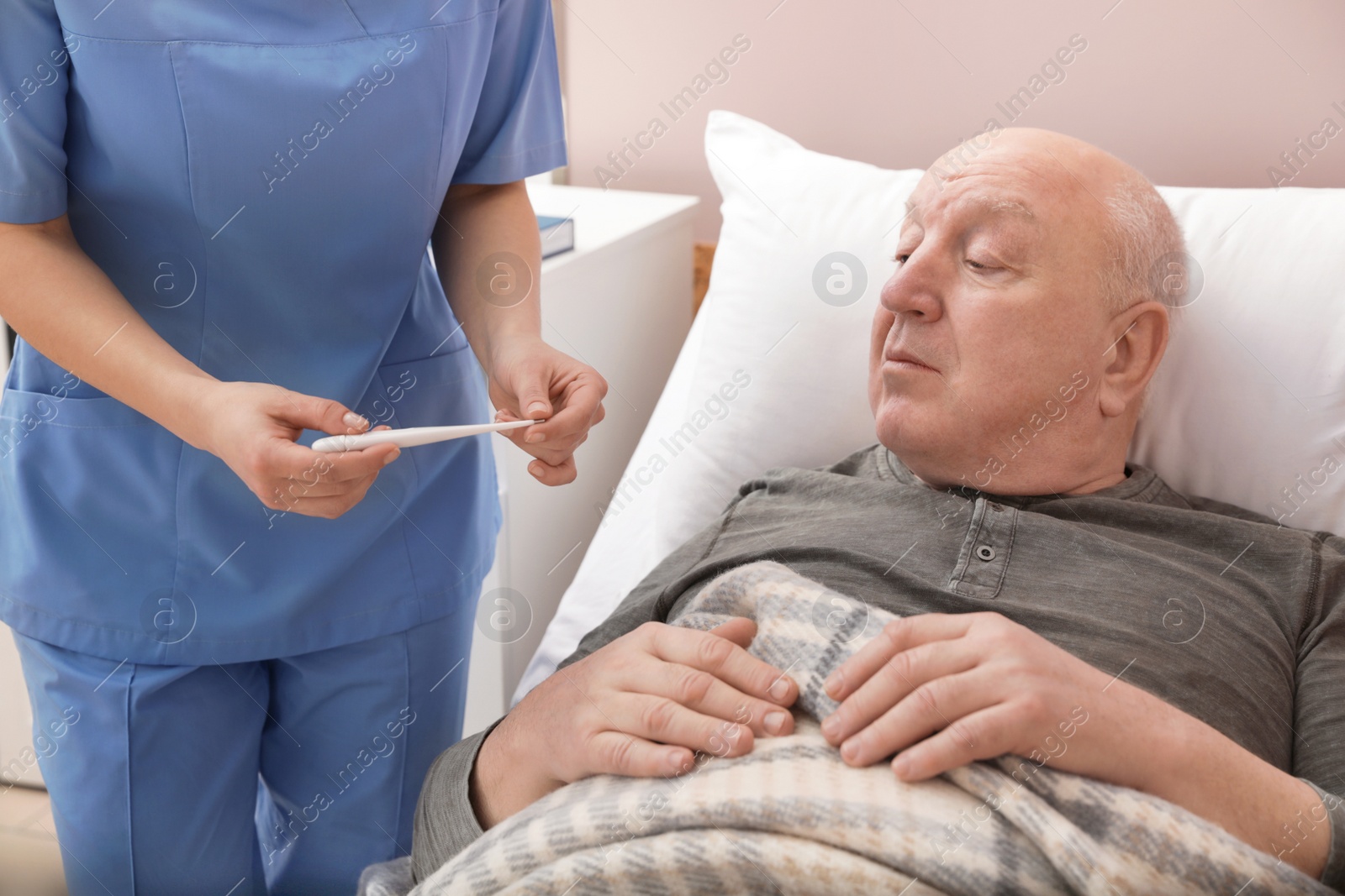 Photo of Nurse measuring senior man's temperature in hospital. Medical assisting