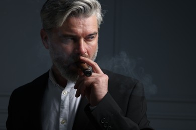 Photo of Handsome bearded man smoking cigar against dark grey background. Space for text
