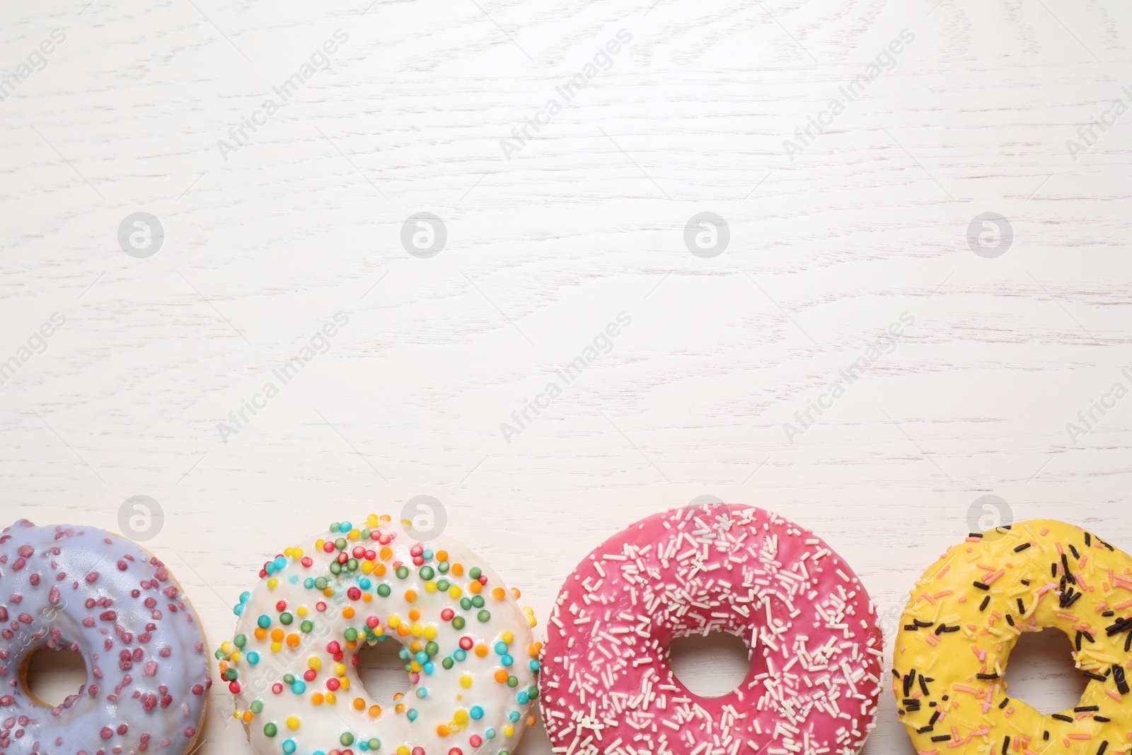 Photo of Delicious glazed donuts on white wooden table, flat lay. Space for text