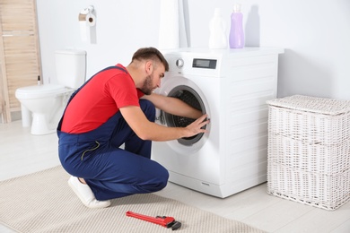 Photo of Young plumber examining washing machine in bathroom