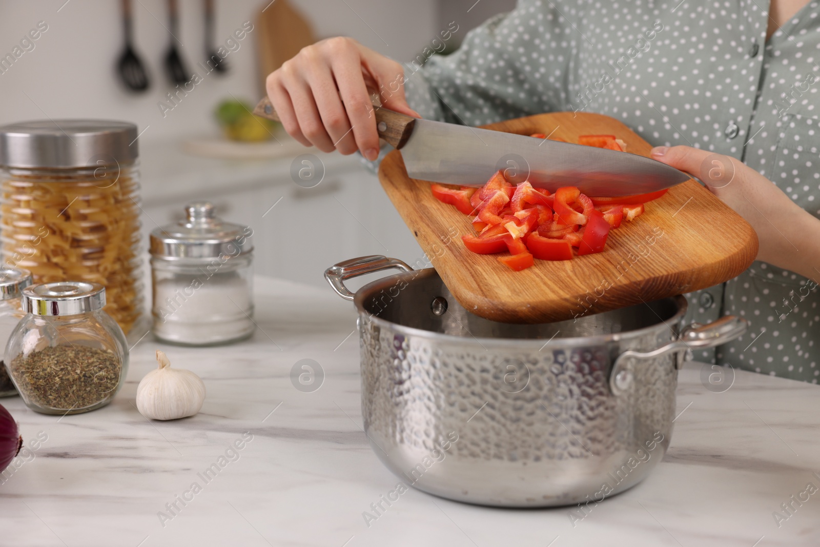 Photo of Cooking process. Woman adding cut bell pepper into pot at white marble table in kitchen, closeup