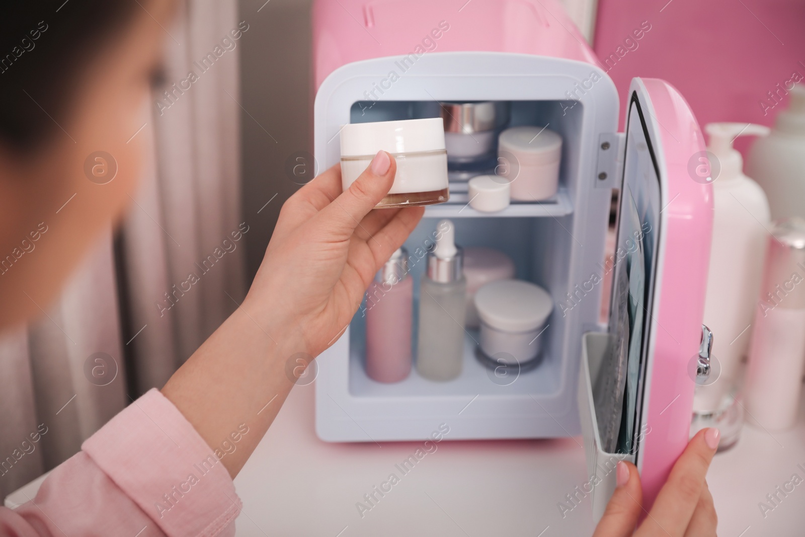 Photo of Woman taking cosmetic product out of mini refrigerator indoors, closeup